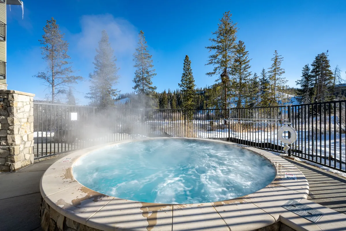 This exterior image features a steaming hot tub surrounded by snow-covered trees and landscape, offering a tranquil spot to unwind after outdoor adventures. The snowy setting and visible steam convey a sense of winter relaxation and après-ski enjoyment.