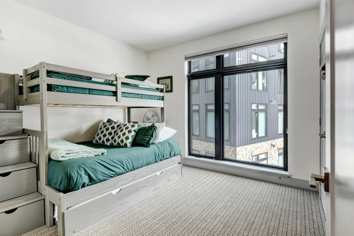 A cheerful bunk bedroom with a twin-over-full bunk bed and trundle, large window for natural light, and playful decorative pillows, offering a cozy and versatile retreat for kids or groups.