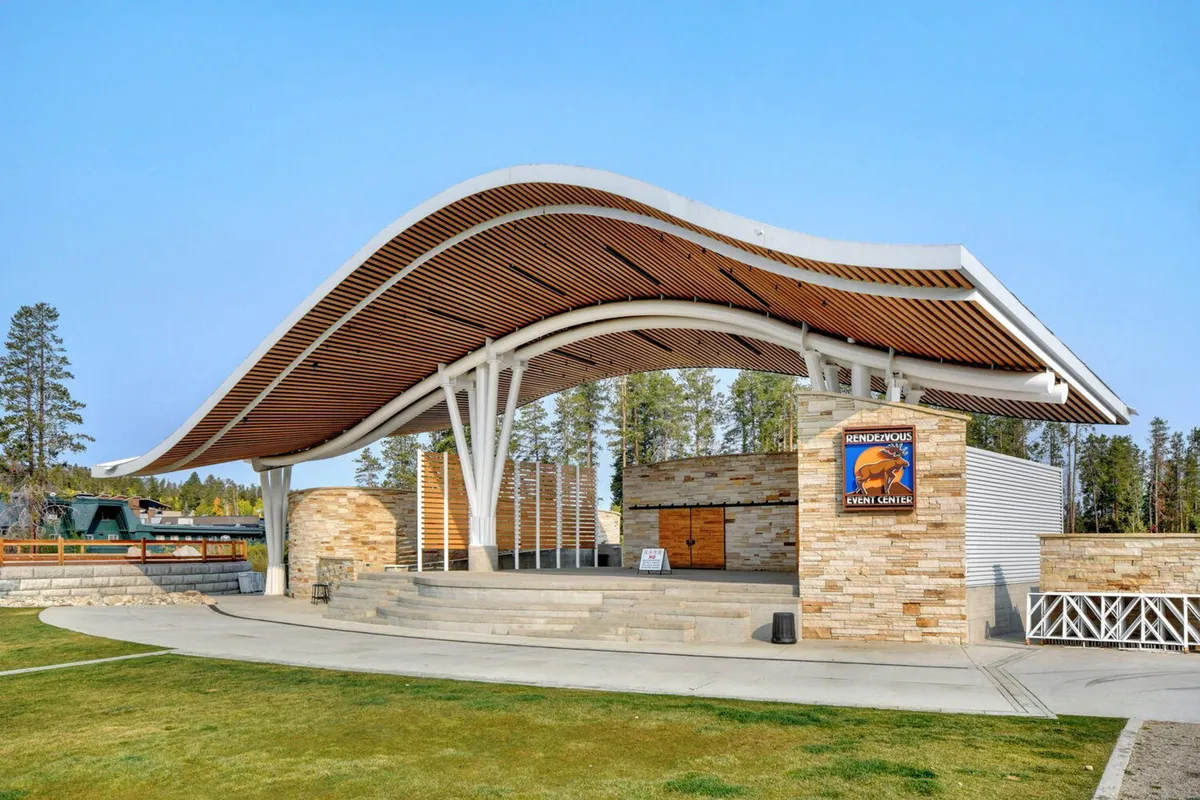An exterior shot highlighting the unique curved roof and open-air stage area of Hideaway Park, inviting visitors to imagine concerts and lively summertime community events. The contemporary design stands out against the natural backdrop.