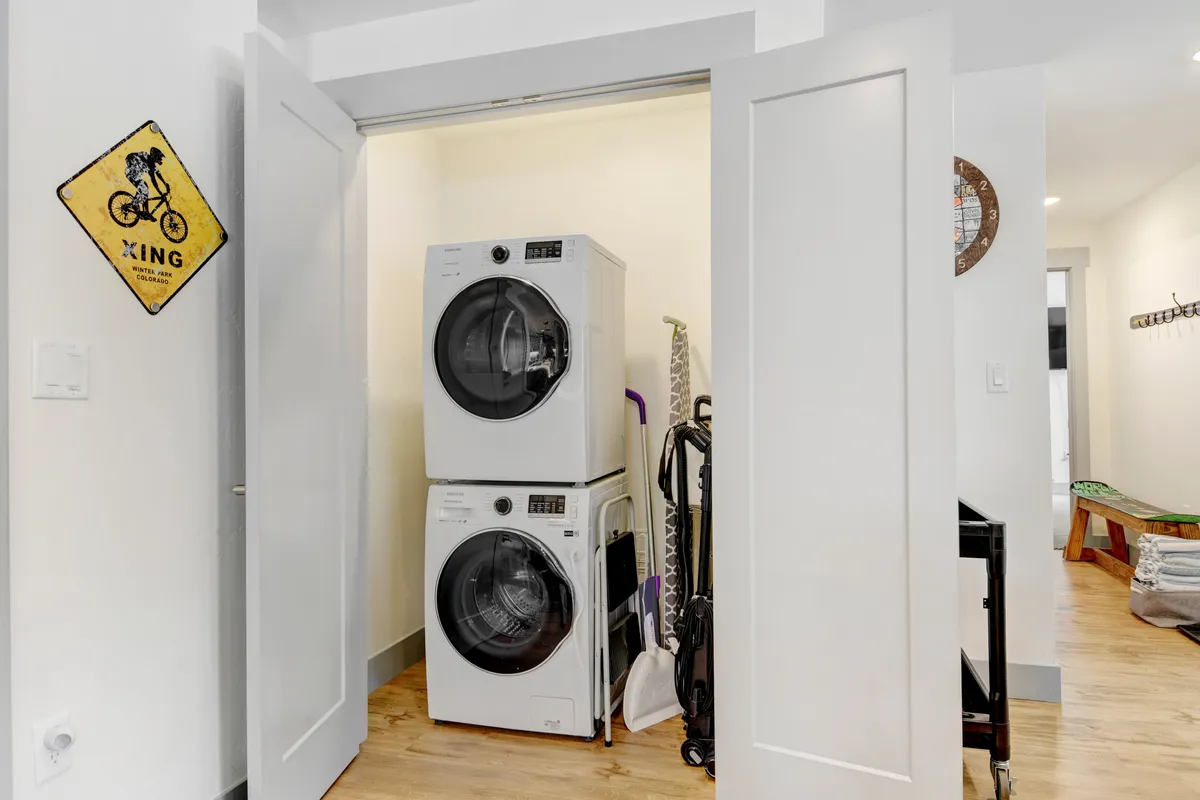 A practical, tidy laundry space featuring a stacked washer and dryer, cleaning supplies, and a playful bicycle crossing sign. The area appears modern and well-organized, supporting convenient in-unit chores for extended stays or active guests.