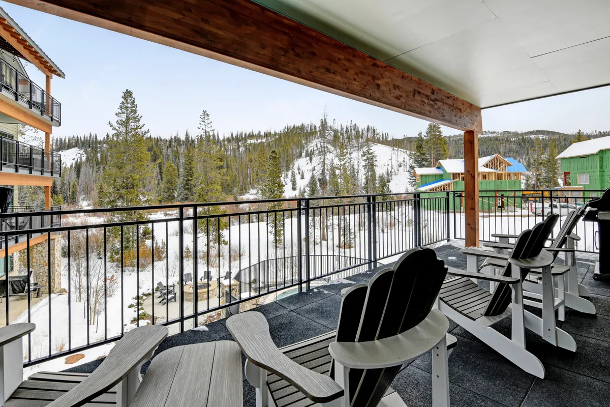 A private balcony furnished with comfortable chairs, overlooking a snow-covered landscape dotted with pine trees and distant mountains. The inviting setting is perfect for morning coffee, outdoor meals, or simply relaxing while taking in the fresh mountain air and scenic views.