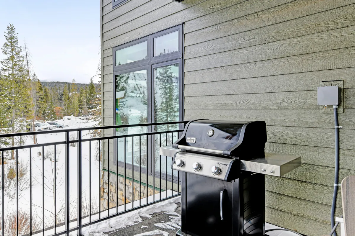 This exterior image shows a snow-covered balcony with a grill and surrounding trees, suggesting both winter coziness and summer grilling potential. The scene balances wintery charm with hints of warmer-season fun, illustrating how the space is enjoyed throughout the year.