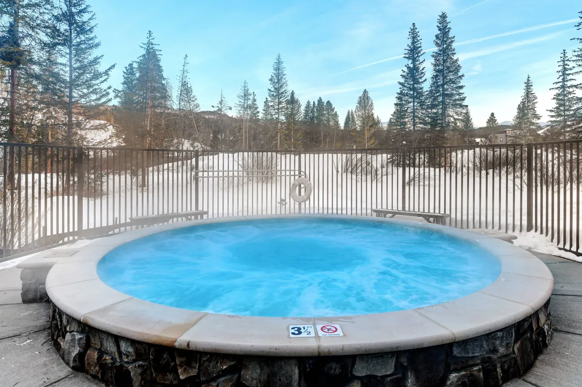 Another tranquil exterior showing a bubbling hot tub surrounded by snow and trees, designed for stargazing or relaxing after a day of adventure. The nighttime ambiance suggests calm and togetherness in nature.