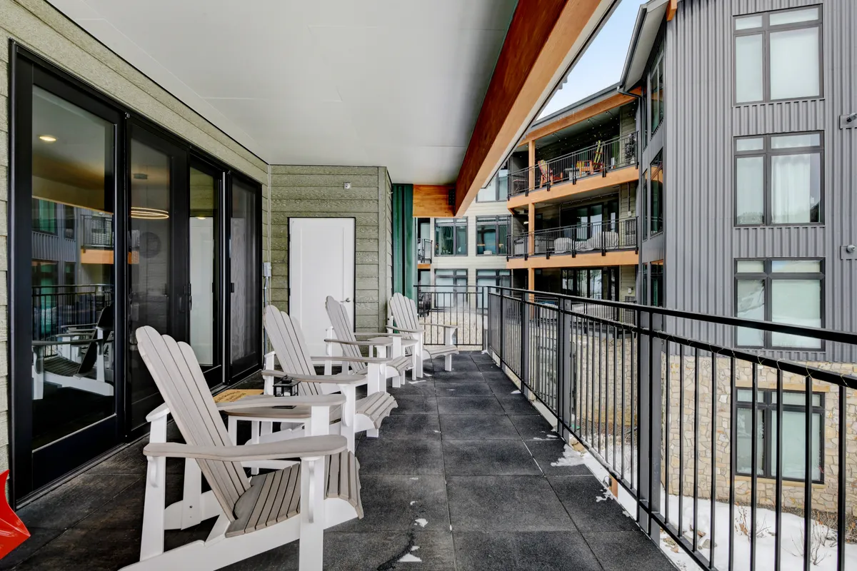 This image features an exterior balcony with Adirondack chairs and a railing overlooking a snow-covered mountain landscape. The setting suggests a tranquil spot to unwind and take in panoramic mountain views, particularly at sunrise or twilight.