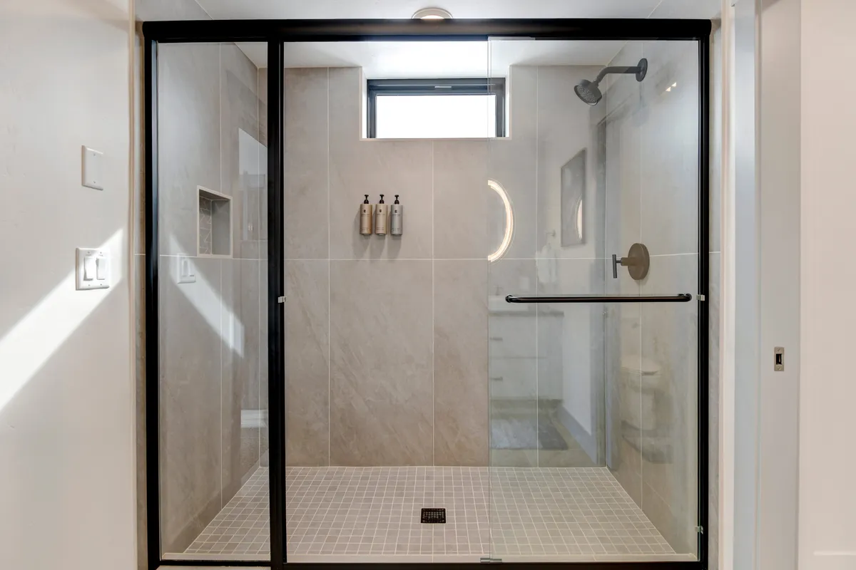 A bright and modern bathroom showcasing a glass shower enclosure with stylish fixtures and natural light streaming through the window, contributing to a spa-like, rejuvenating atmosphere.